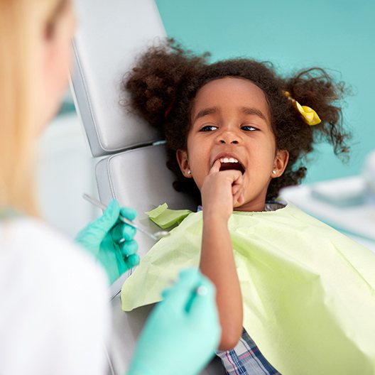 Little girl at emergency dentistry visit pointing to her smile