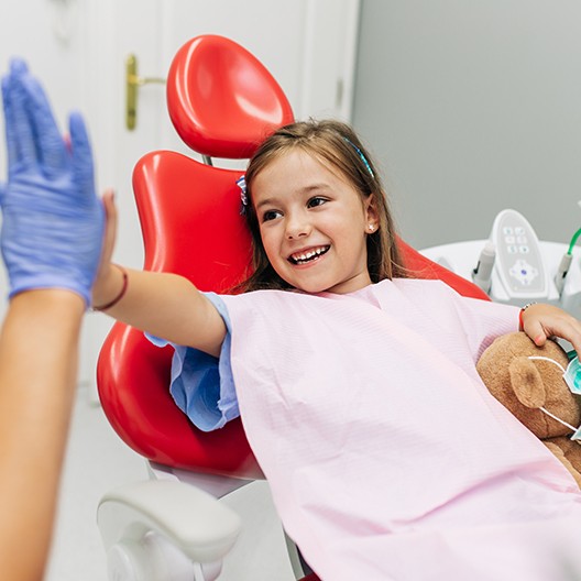 Little girl in dental chair giving dentist a high five
