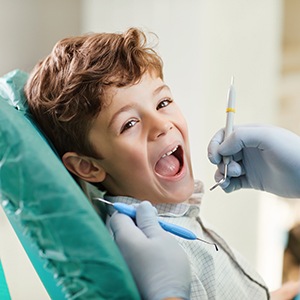 Little boy in dental chair holding mouth open for dentist