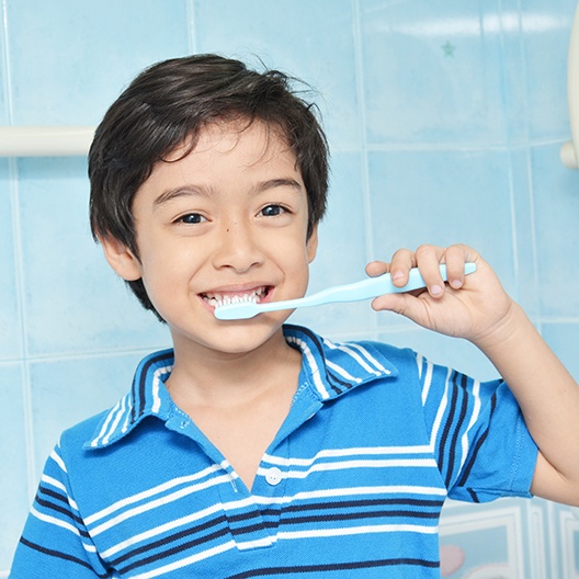 Little boy in striped blue shirt brushing his teeth