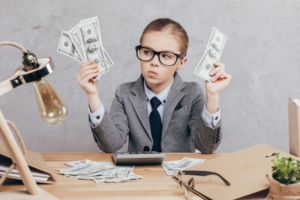 Professionally dressed child sitting at desk and holding money